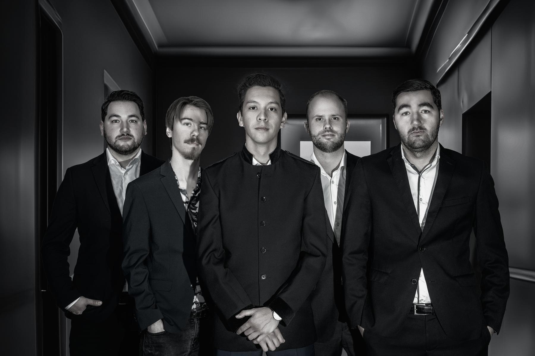 The band in black suits in a dark corridor